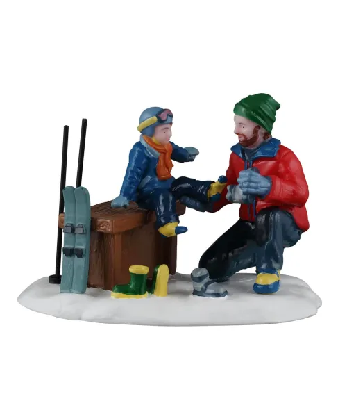 Lemax Father and Son Ski Day 62633: papà aiuta il figlio a indossare gli scarponi da sci